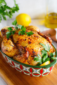 Whole roasted chicken with fresh parsley and lemon wedges in a festive dish