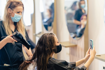 Hairdresser drying her clients hair with a hairdryer wearing protective masks in a beauty centre