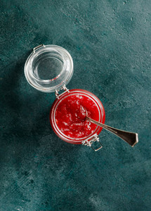 Top view of strawberry jam in a glass jar on a green background