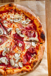 Top view of pizza with prosciutto and champignons on a wooden background