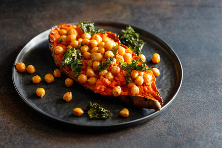 Baked sweet potato stuffed with chickpea and crunchy kale on a black plate Vegan tasty dish for dinner or lunch