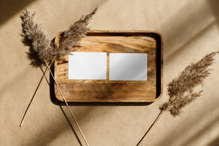 Top view of two blank paper sheet cards on a wooden tray with dry grass Beige or sand tones Mockup for business template copy space