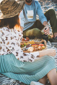Young couple having picnic with sparkling wine fruit and snacks