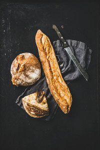 Flat lay of freshly baked baguette and loaf over black background