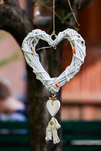 The decorative wicker white heart is hanging on a tree