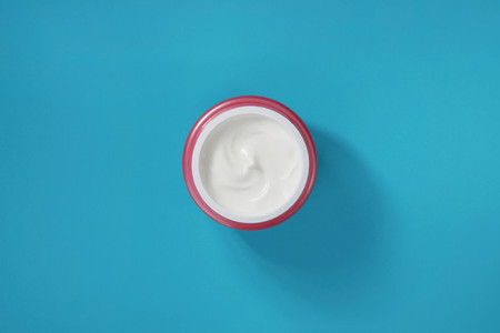 White cream for skin in a pink container on a blue background  View from above