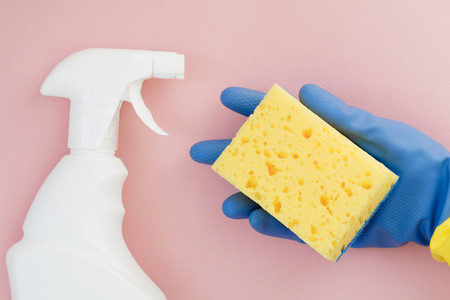 Hand in a blue rubber glove holds a yellow sponge for cleaning on a pink background  Flat lay