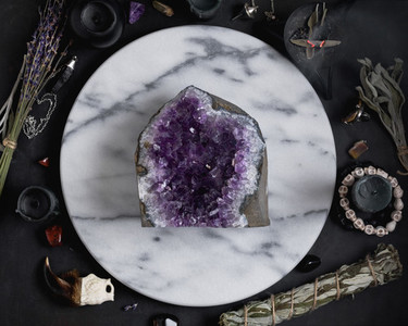 Druze of amethyst stone surrounded magic things on the round white marble tray  View from above