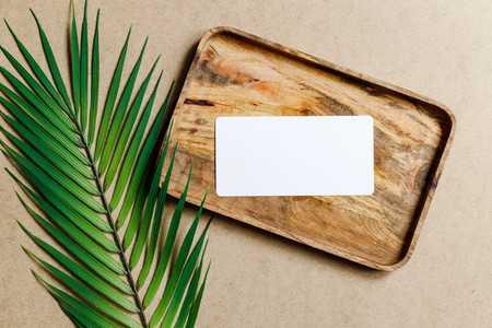 Top view of a blank paper sheet card on a wooden tray with palm leaf  Summer mockup for business template  copy space