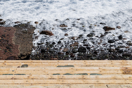 View of wooden stairs on the coast with rocks and sea foam