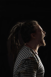 Angry man with dreadlocks screaming against black background