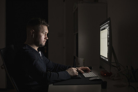 Man with earbuds working late at computer in dark room