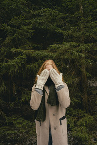 Portrait playful woman with mittens covering face in woods