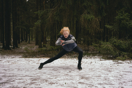 Athletic female runner stretching in snowy woods