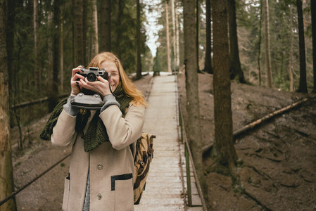 Portrait woman using retro camera on footbridge in woods