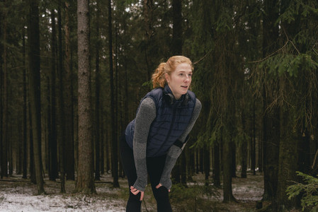 Female runner resting with hands on knees in snowy woods