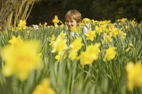 Portrait happy boy enjoying Easter egg hunt in field of yellow daffodils