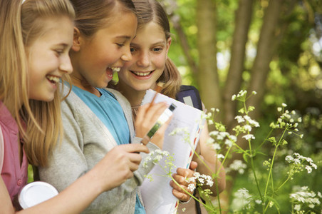 Smiling girls with magnifying glass examining flowers on field trip