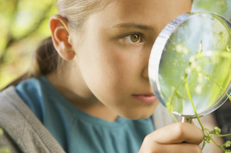 Close up curious girl with magnifying glass examining plant