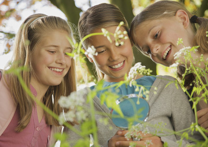 Smiling curious girls with magnifying glass examining flowers