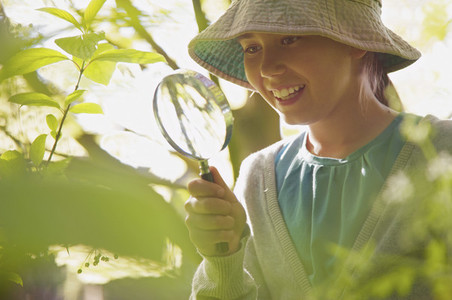 Smiling curious girl with magnifying glass examining plants