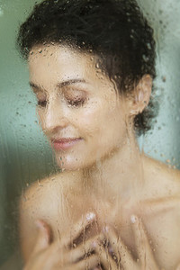 Sensual woman taking a shower behind wet glass