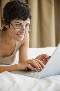 Woman online shopping with credit card and laptop on bed
