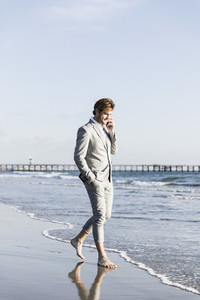 Barefoot businessman talking on smart phone on sunny ocean beach