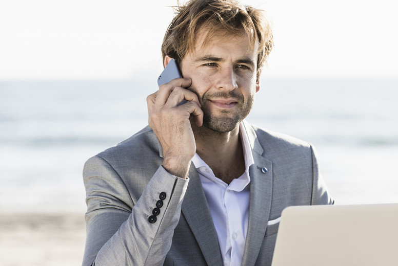 Businessman with smart phone and laptop working on sunny beach