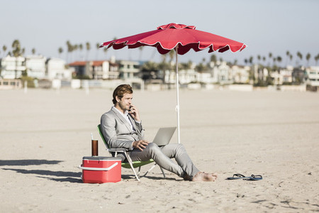Barefoot businessman working on sunny beach
