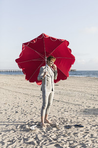 Barefoot businessman with beach umbrella on sunny beach