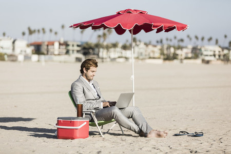 Barefoot businessman using laptop on sunny beach  Los Angeles