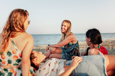 Young women lying on beach  smiling and talking over big scarf