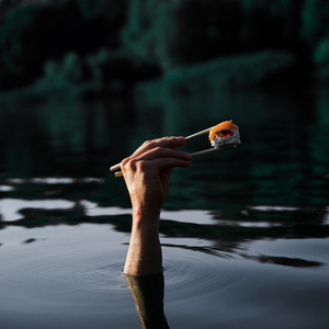 Sushi with wooden chopsticks in male hand on water background