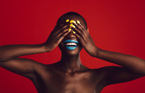 Cheerful woman with vibrant makeup covering her eyes