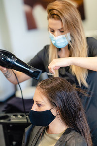 Hairdresser drying her clients hair with a hairdryer wearing protective masks in a beauty centre