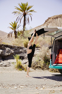 Young active woman practicing yoga in desert on sunny day  with a campervan