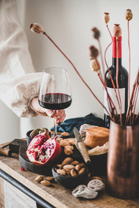 Womans hand holding glass of red wine over various snacks