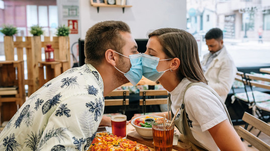 Couple kissing with mask sitting in a restaurant