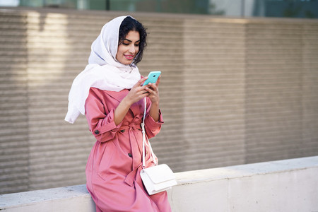 Young Muslim woman wearing hijab texting message with her smartphone