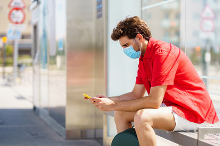 Young man wearing a surgical mask while waiting for a train at an outside station