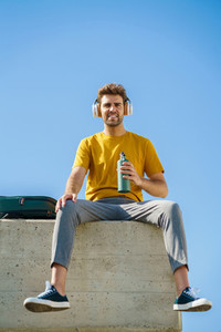 Male sitting outside using an aluminum water bottle headphones and backpack