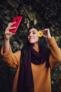 Woman taking a selfie with her phone with flower in her hair