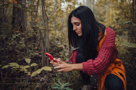 Woman taking photos with her phone through the forest