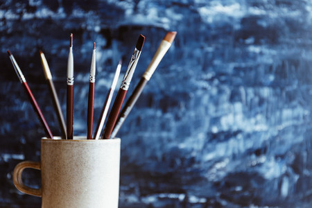Painting brushes in a ceramic mug against a blue abstract background
