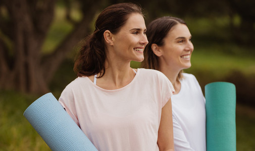 Fitness women standing outdoors holding yoga mats
