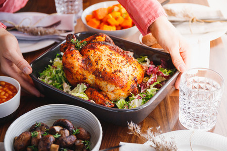 Hands put a dish with whole roasted chicken on a festive table The concept of family dinner or Thanksgiving celebrate