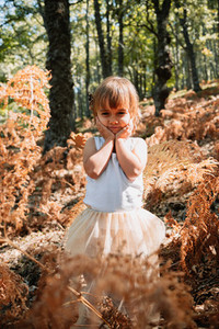 Little caucasian baby girl squatting in the forest among ferns