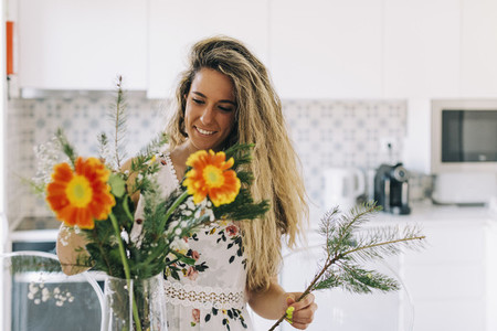 Smiling young woman arranging flower bouquet in kitchen