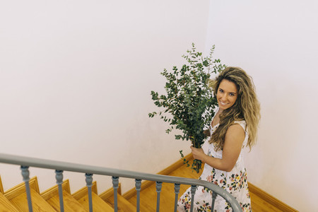 Portrait smiling woman carrying bunch of eucalyptus on staircase